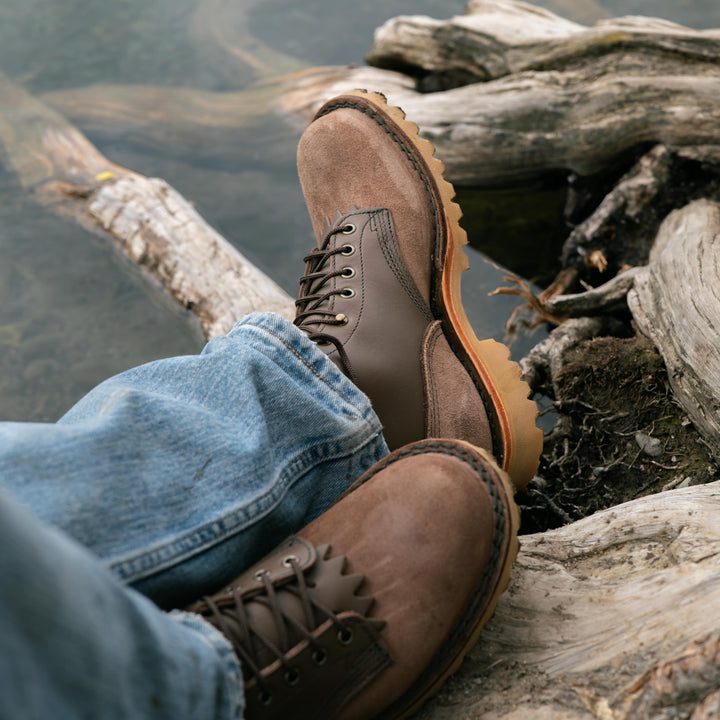 Pair of OT Mocha leather work boots worn by a person on a log and next to water