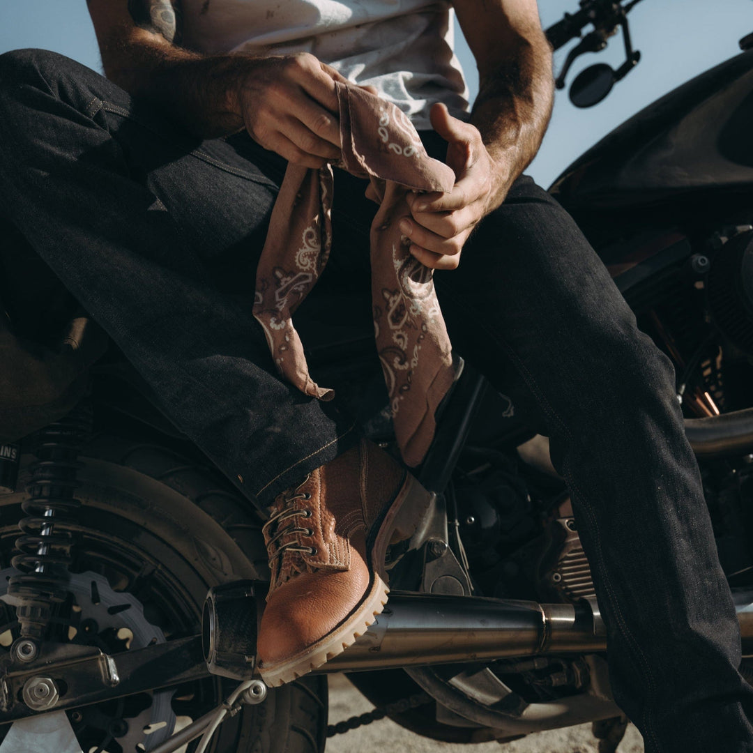 Person sitting on a motorcycle wearing OT Canyon Bison leather work boots and holding a bandana.